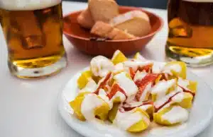 Plato de patatas bravas acompañado de una caña de cerveza en una mesa de bar sevillano. Tapas Sevilla